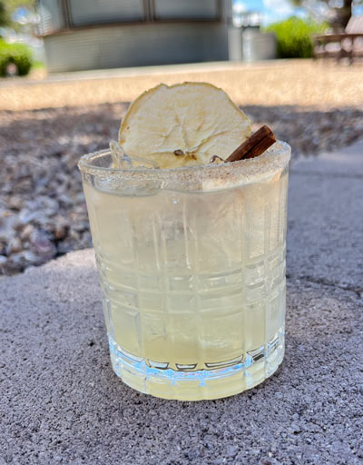 Cinnamon Sugar Rim. Shaken and poured into rocks glass. Garnished with Apple Chip and Cinnamon Stick